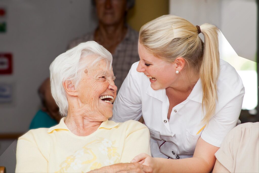 Junge Pflegerin lacht mit alter Frau